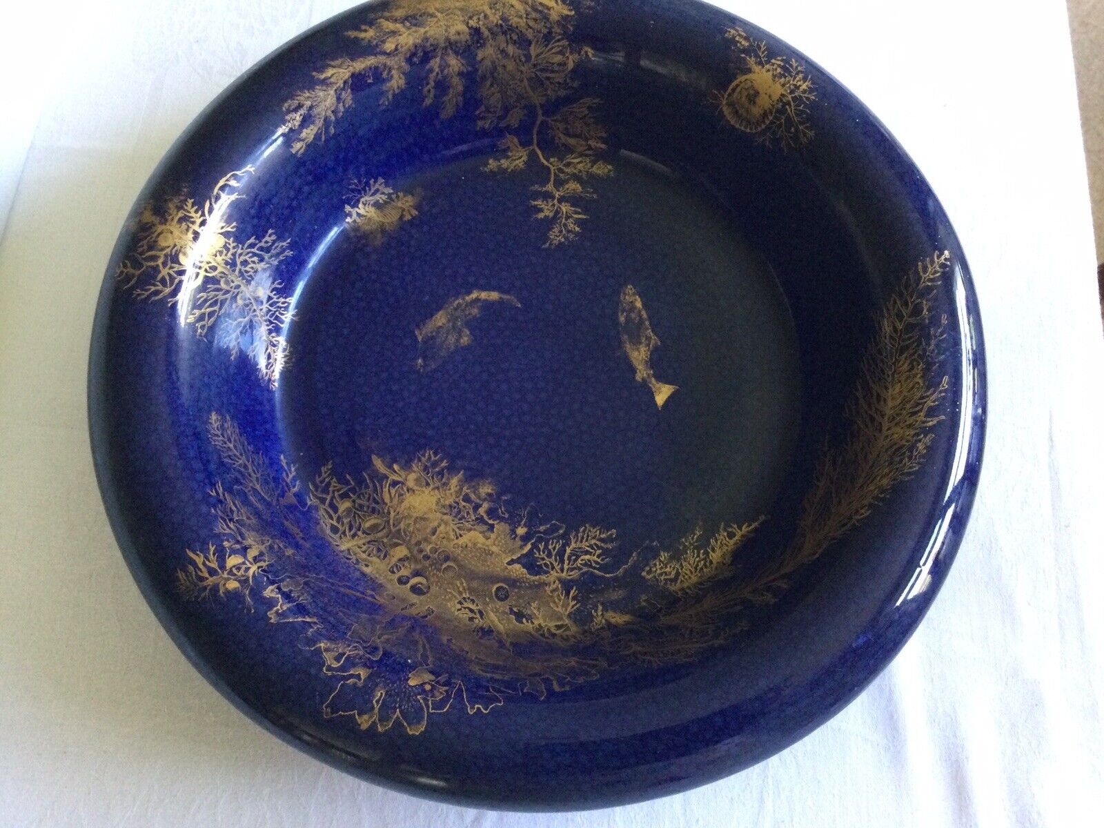 antique large earthenware bowl blue with gold lustre fish, seaweed and trees.